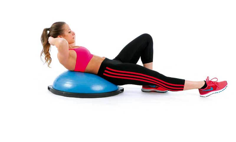 Recuéstate tu espalda sobre el bosu y comienza a hacer flexiones abdominales subiendo un poco el tronco.