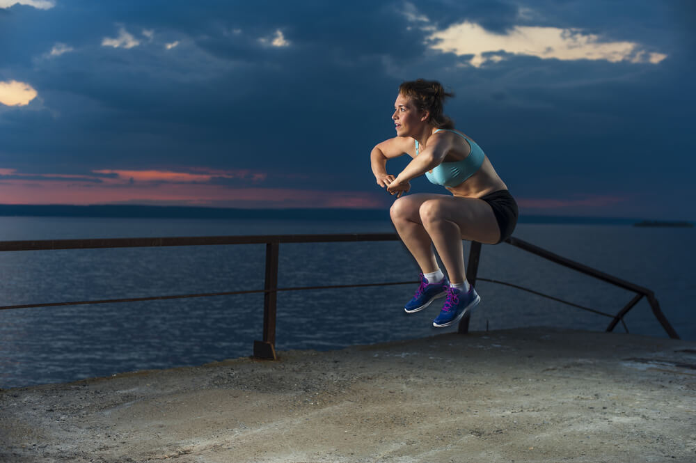 Mujer realizando salto rodilla al pecho para entrar en calor.