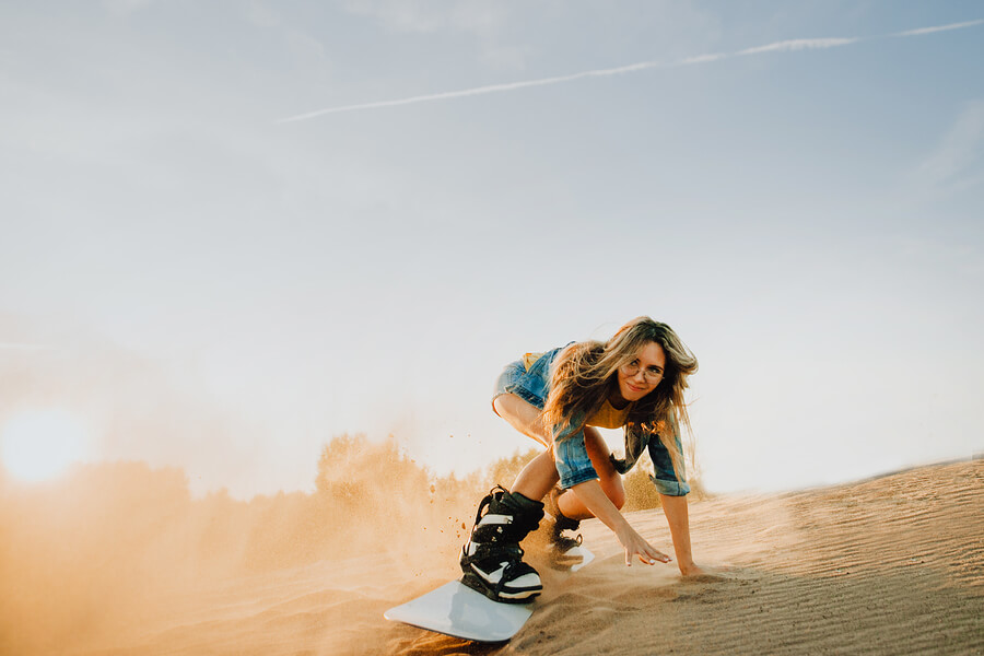 Joven haciendo sandboard en el desierto.