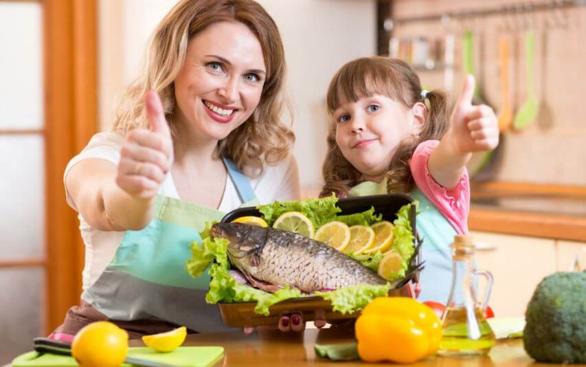 Madre e hija preparando receta saludable con pescado.