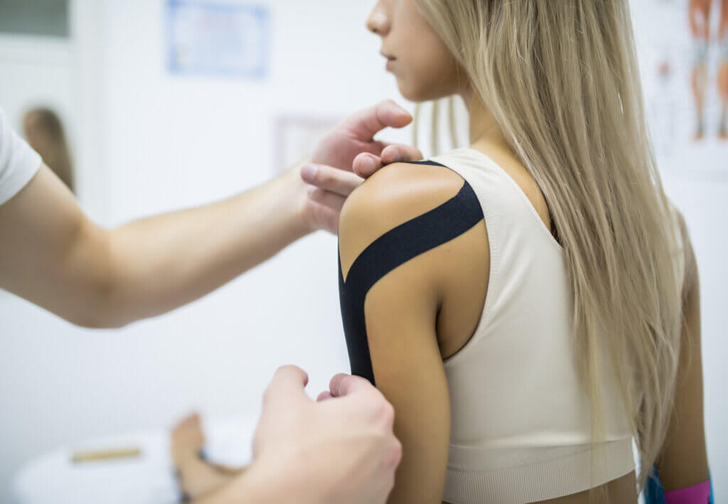 Fisioterapeuta aplicando vendaje neuromuscular en brazo de mujer joven.