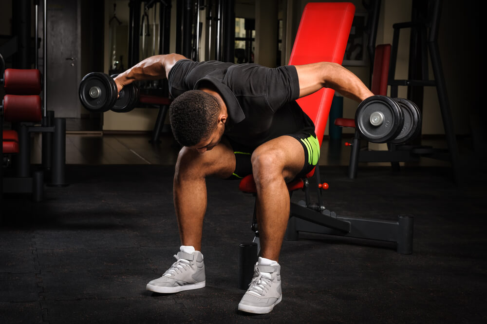 Joven haciendo pájaros en el gimnasio para obtener superhombros.