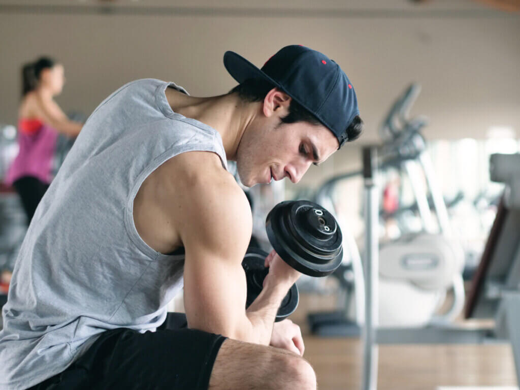 Joven haciendo curl de bíceps en gimnasio para hipertrofiar.