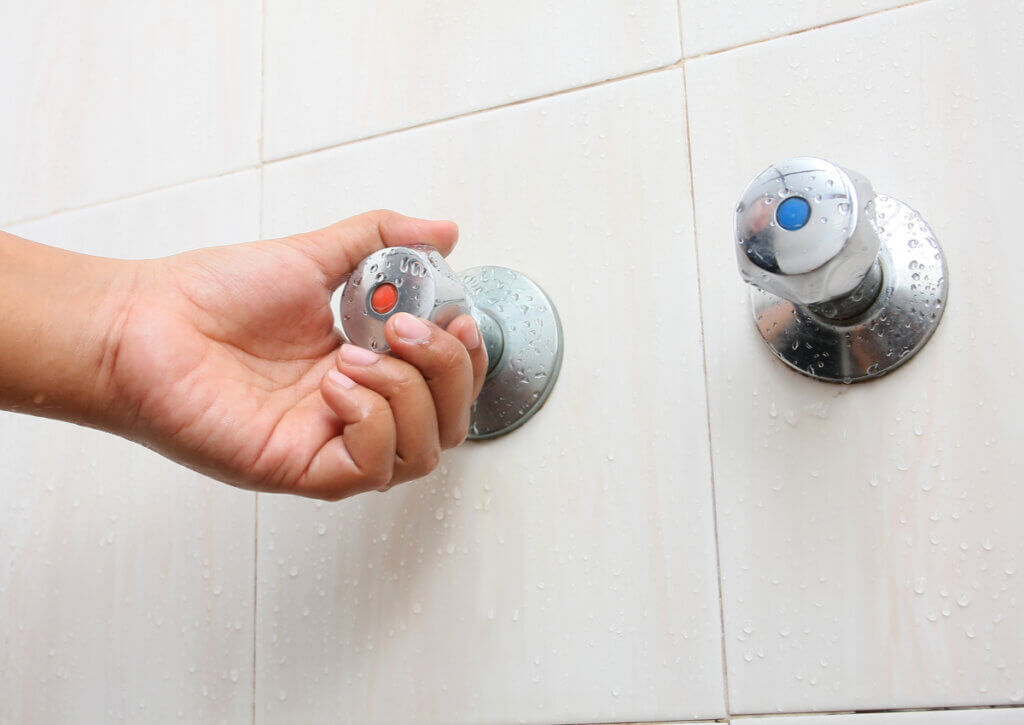 Manejando grifería de la ducha para ducharse con agua fría.