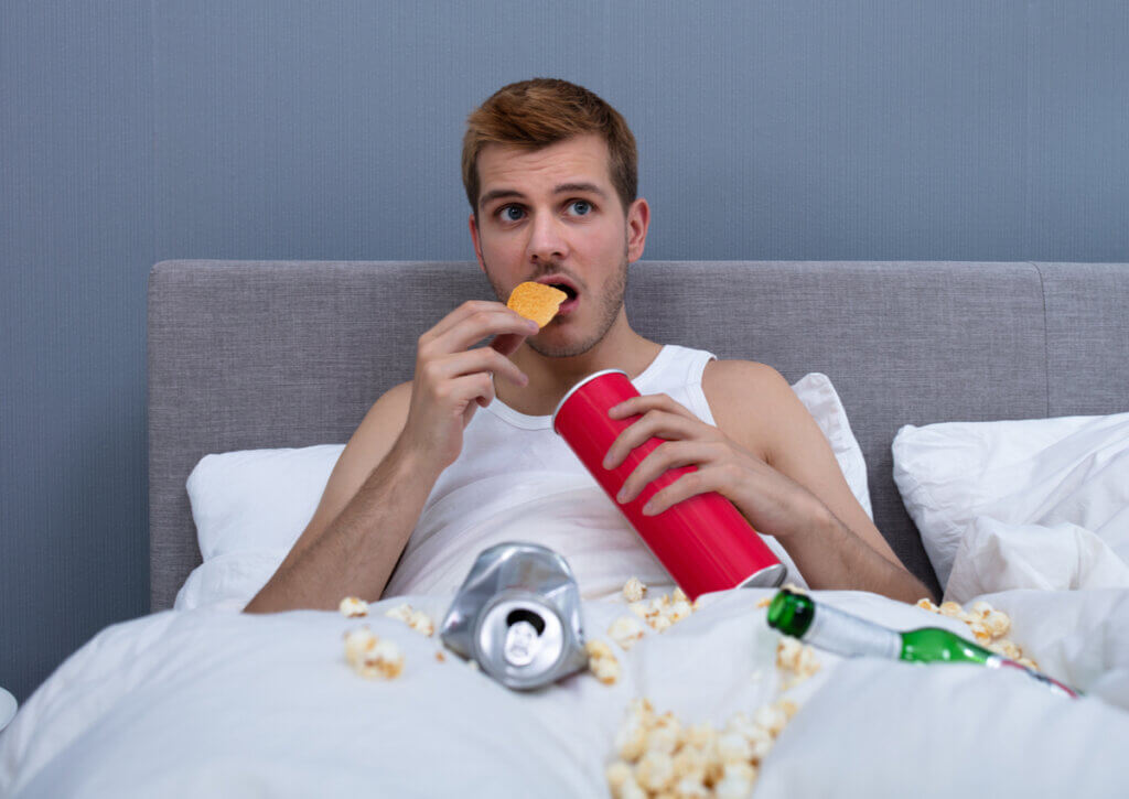 Joven comiendo comida chatarra en la cama.