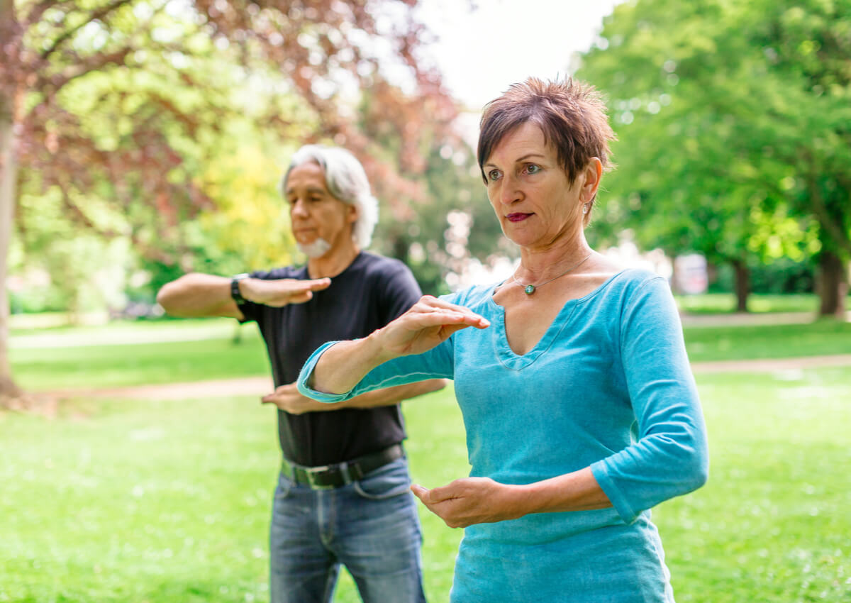 Pareja de personas mayores haciendo taichí en el parque.