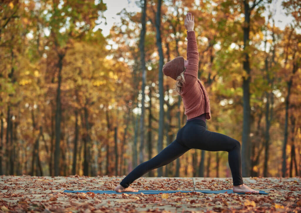 Mujer realizando yoga al aire libre con un paisaje otoñal.