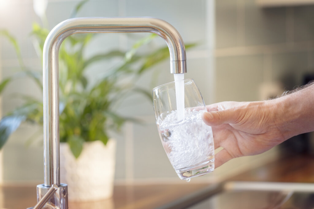Mujer llenando vaso de agua con el grifo.