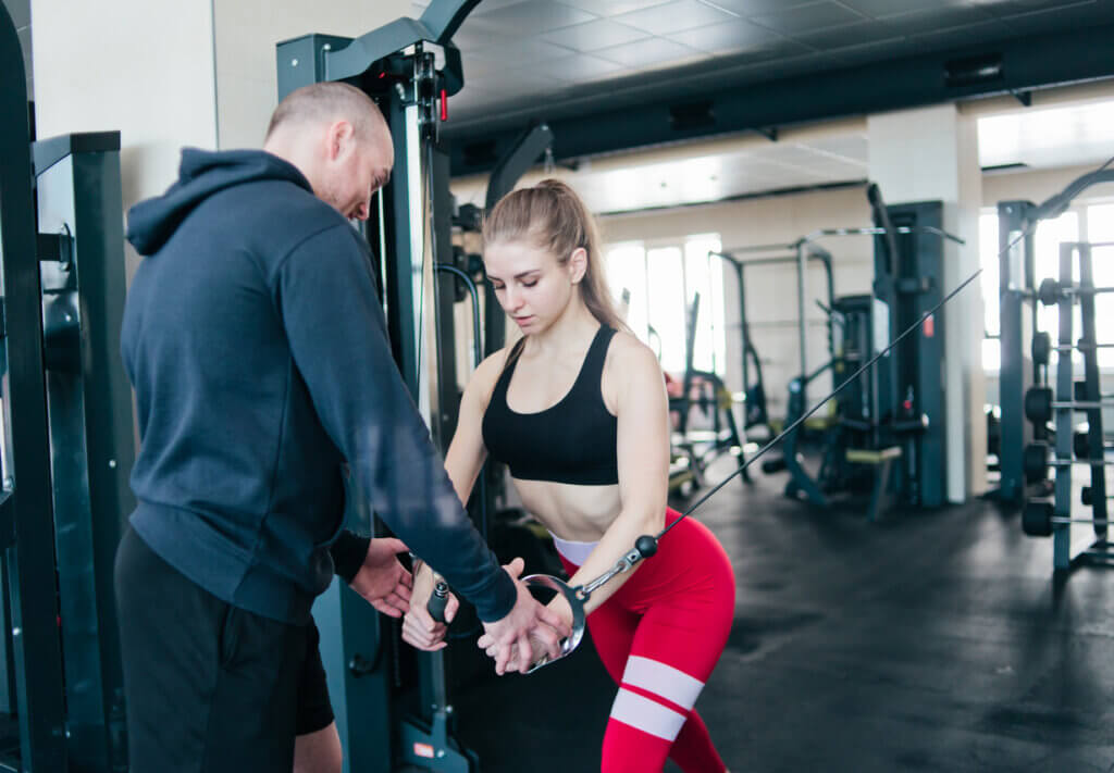 Entrenador le enseña a alumna a trabajar los cruces en polea alta para los pectorales.