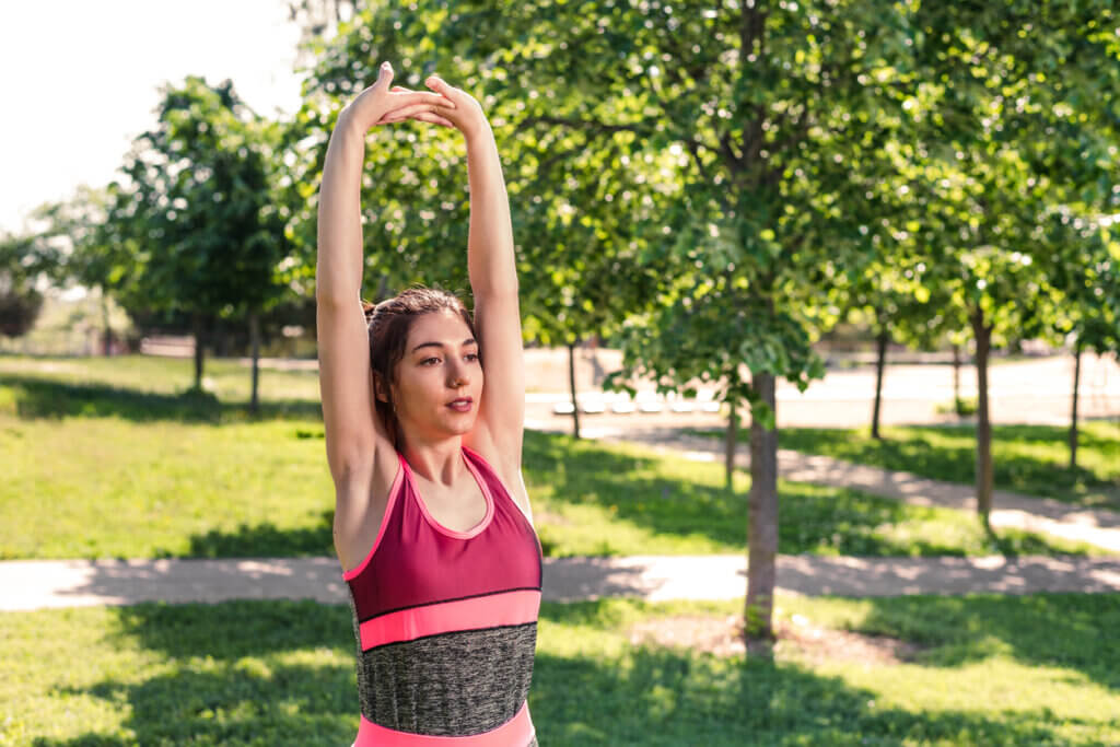 Mujer realizando estiramiento del músculo dorsal ancho al aire libre.