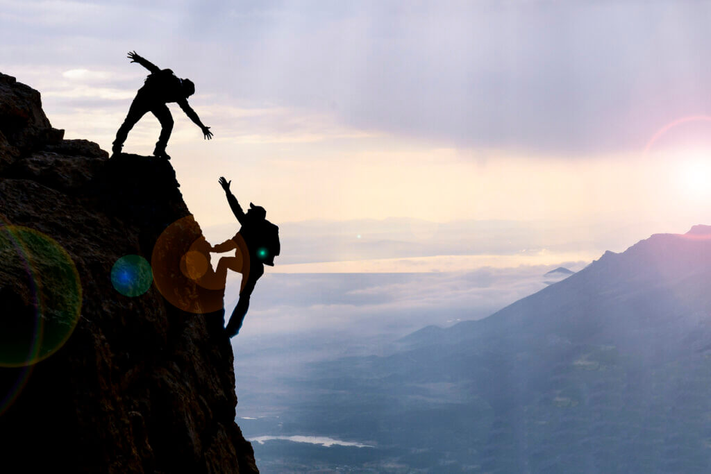 Personas que escalan una montaña ayudándose en una muestra de empatía