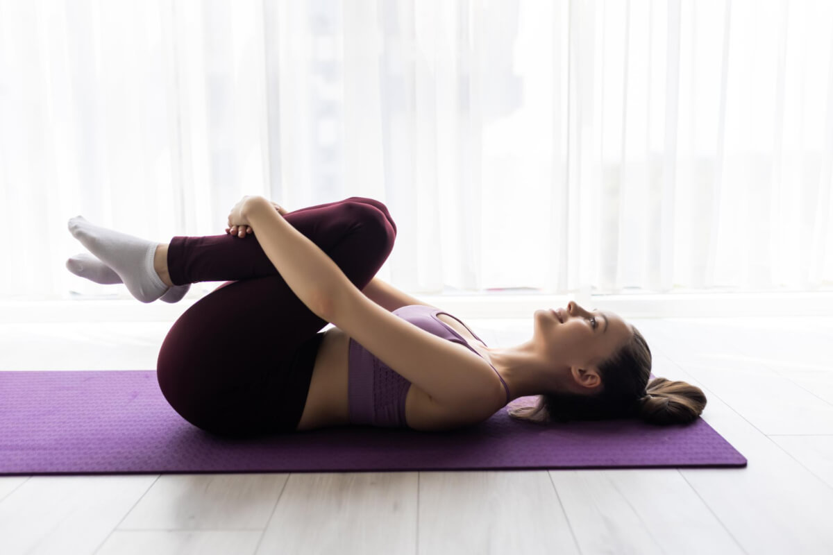 Mujer ubicando sus rodillas en el pecho como ejercicios para relajar la zona lumbar